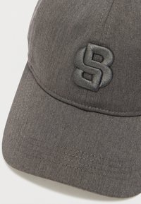 Șapcă gri cu model în chevron, cu bor curbat și logo negru brodat, în relief, pe față. Țesătură texturată cu cusături vizibile.