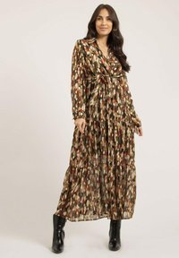 Robe longue à motifs dans des tons terreux avec un col, une taille ceinturée et une jupe à volants. Fabriquée en matériau léger et fluide. Bottines noires à la cheville.