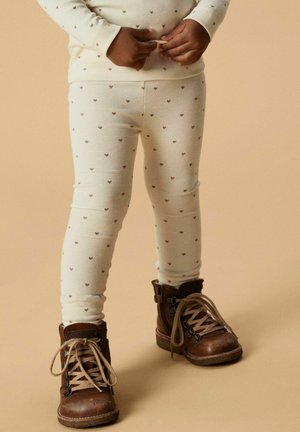 Leggings crème avec de petits motifs de cœurs multicolores, associées à des bottes marron en cuir à lacets avec des accents métalliques et une surface texturée.