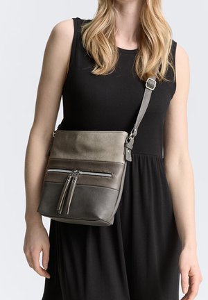 Mujer vistiendo un vestido negro sin mangas con un bolso cruzado que presenta tres bloques de color horizontales en tonos grises y marrones.