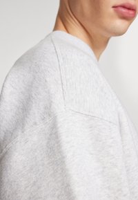 Sweatshirt gris en mélange de coton doux, avec une coupe décontractée, des détails de couture visibles et un col rond. Surface de tissu texturé.