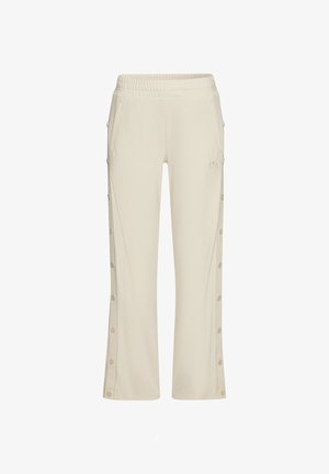 Pantalon de lounge beige clair avec une taille élastique, poches latérales et détails de boutons le long des coutures extérieures. Le tissu a une texture douce.
