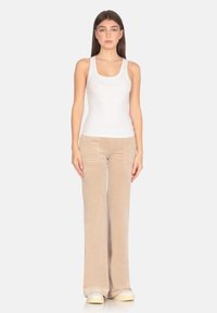 Canotta bianca con texture a coste e testo ricamato, abbinata a pantaloni a zampa in velluto beige e sneakers di colore chiaro.