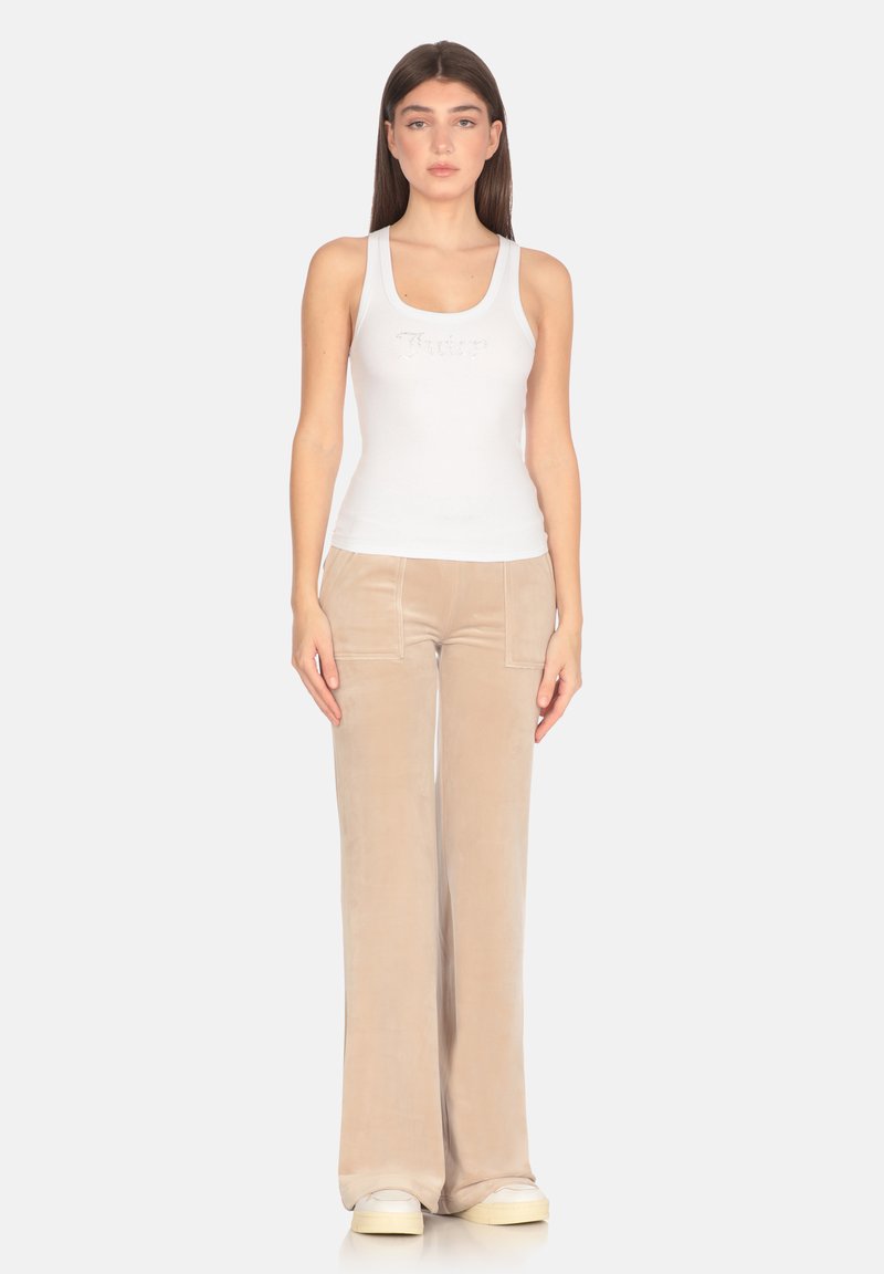 Canotta bianca con texture a coste e testo ricamato, abbinata a pantaloni a zampa in velluto beige e sneakers di colore chiaro.