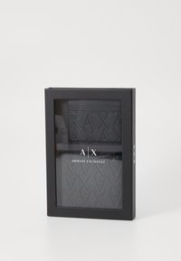 En svart gaveeske inneholdende et strukturert svart lommebok og kortholder. "AIX ARMANI EXCHANGE"-logoen vises tydelig på forsiden av lommeboken.