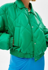 Zelená prošívaná bunda s límečkem, snap knoflíky a elastickými manžetami, se boční kapsou a lesklým povrchem.