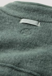 Grijze stevig gevoelde stof met een gladde textuur, met een klein reliëflogo en een gestikt stoffen label bij de halslijn.