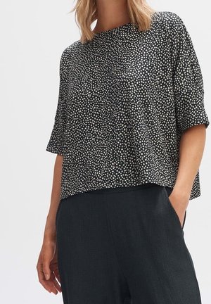 Czarna i biała bluzka w wzory o krótkich rękawach, okrągłym dekolcie i luźnym kroju, zestawiona z ciemnymi, textured spodniami.