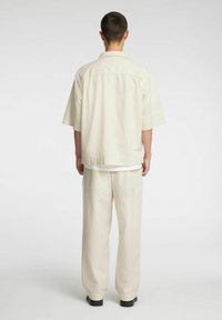 Jasna, oversize'owa koszula z krótkim rękawem i spodnie o szerokich nogawkach wykonane z miękkiej tkaniny. Posiadają swobodny krój i dyskretne kieszenie.