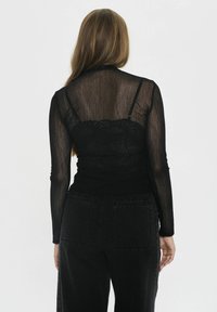 Top negro transparente de manga larga, superpuesto a un sujetador de encaje negro, combinado con unos pantalones vaqueros ajustados negros de cintura alta, que cuentan con bolsillos traseros.