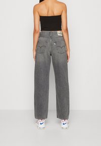 Breda grå jeans med vida ben, fem fickor, kontrasterande sömmar och en läderlogotyp på midjebandet. Bärs med vita sneakers.