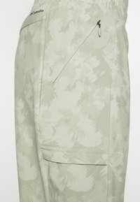 Ljust gröna byxor har ett blommönster, elastisk midja och en ficka med dragkedja på höger sida för säker förvaring.