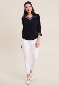 Maglione blu navy con colletto a fantasia e maniche a tre quarti, abbinato a pantaloni bianchi slim-fit e sneaker bianche con tre strap.