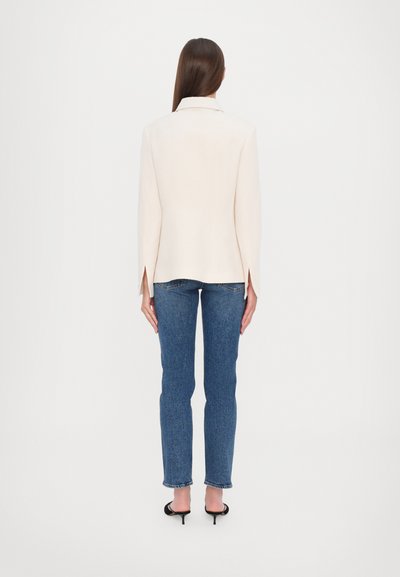 Light beige blazer with a classic collar, side slits, paired with dark blue jeans and black heeled sandals. Minimalist design.