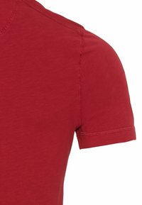 T-shirt rosso a maniche corte con scollatura rotonda, caratterizzato da una trama sottile e cuciture pulite lungo i bordi.