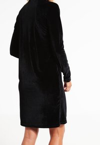 Schwarzes Samtkleid mit langen Ärmeln, das eine lockere Silhouette und einen mittellangen Schnitt aufweist, mit glatter Textur und schlichtem Design.