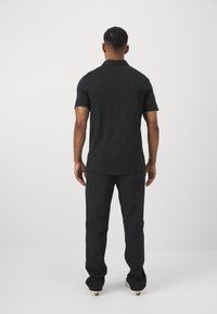 Polo negru cu mânecă scurtă, croială dreaptă și material moale; asortat cu pantaloni negri cu o croială lejeră și un design minimal.