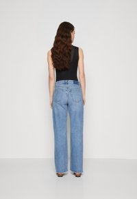 Light blue wide-leg jeans with a frayed hem and five pockets, made of denim, shown from the back against a plain background.
