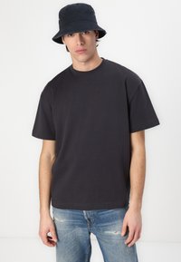 Black short-sleeve t-shirt with a round neckline, paired with light blue distressed jeans and a black bucket hat. Simple, casual design.
