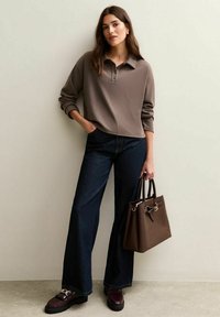 Brązowy sweter z kołnierzykiem, ciemnoniebieskie szerokie dżinsy, czarne platformowe loafersy, trzymając brązową skórzaną torebkę z złotymi akcentami.