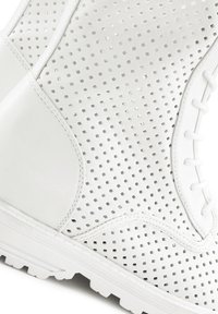Bílé perforované kožené boty s čtvercovými výřezy, hladkými texturovanými akcenty a bílou gumovou podrážkou s detailním vzorem podrážky.