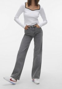 Camisa blanca de manga larga con escote cuadrado y ribete negro, combinada con jeans de pierna ancha grises de talle alto y zapatillas blancas con acentos rojos.