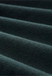 Tessuto in un intenso teal scuro con una lieve ribatura, che mostra pieghe e una superficie morbida, leggermente pelosa. Ideale per diverse applicazioni tessili.