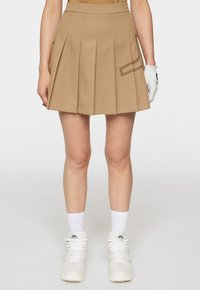 Tan plisserad kjol med en jämn textur och en sidficka. Kombinerad med vita högklassiga sneakers och strumpor.