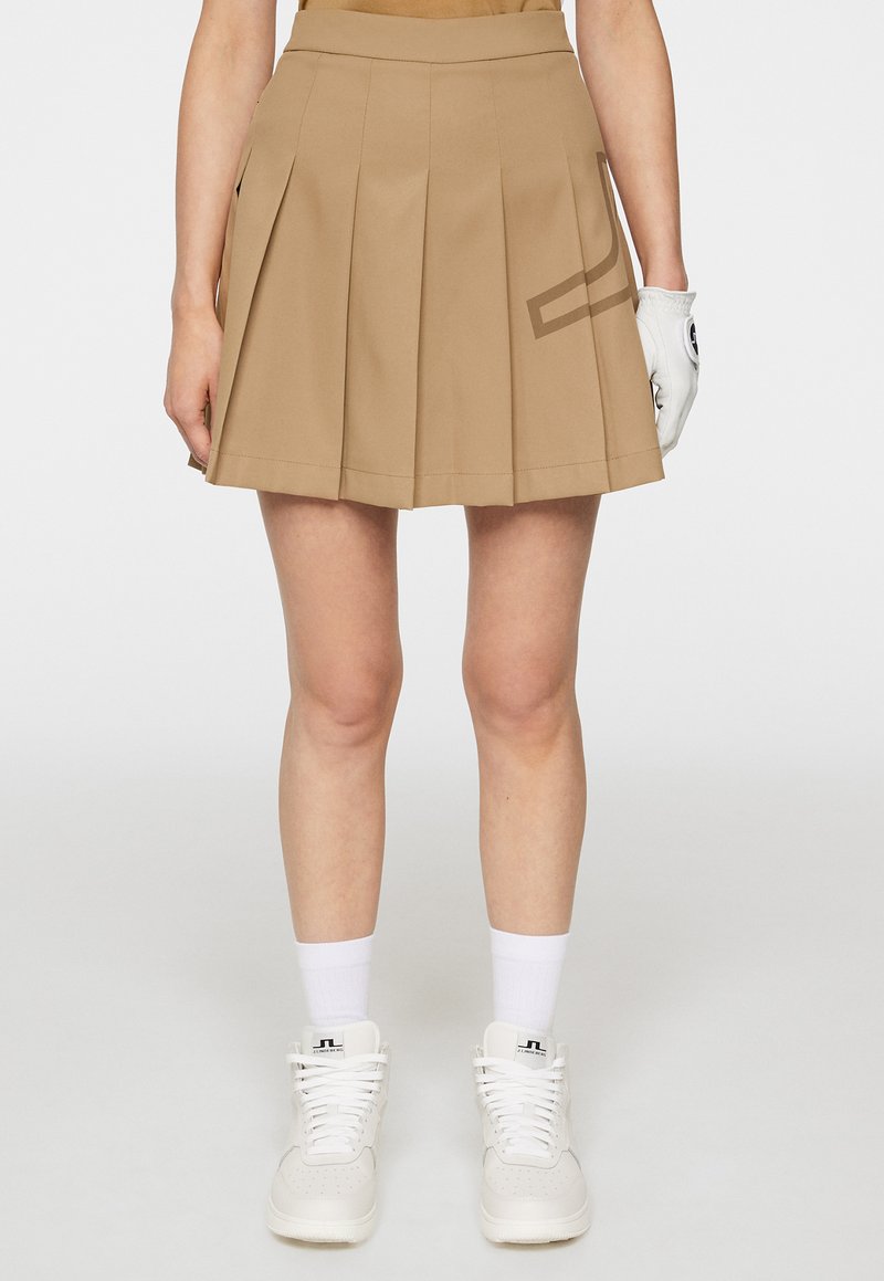 Tan plisserad kjol med en jämn textur och en sidficka. Kombinerad med vita högklassiga sneakers och strumpor.