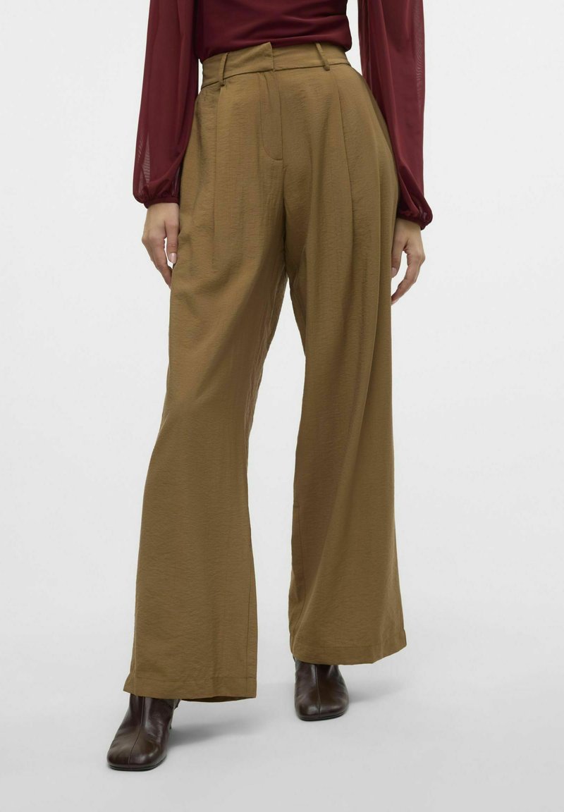 Pantalons larges marron en tissu texturé, avec des plis et une taille haute, associés à des bottines chelsea marron foncé.