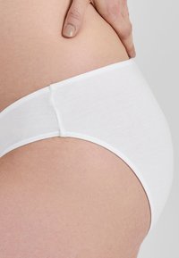 Balti medvilniniai hipster stiliaus apatiniai, turintys lygų paviršių ir elastingą juosmenį, pasižymintys paprastu dizainu, be matomų raštų ar aksesuarų.