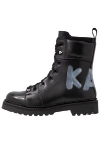 Stivaletto nero in pelle con design allacciato, dotato di accenti metallici e lettere bianche dipinte "KA" sul lato. Suola spessa e testurizzata.