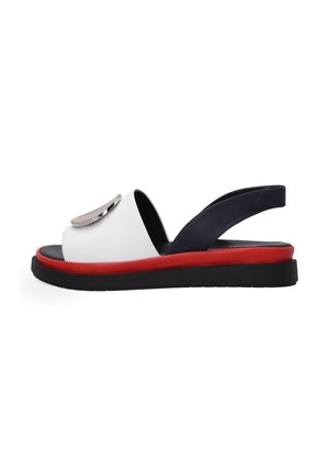 White sandal with a rounded front, black sole, red platform, and navy back strap; features a metallic circular accent on the front.