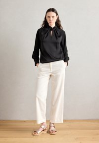 Black satin blouse with a tied neckline, long sleeves, paired with cream wide-leg pants, and beige wedge sandals with adjustable straps.