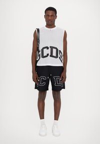 Top senza maniche bianco in rete con grafica nera "GCDS", abbinato a pantaloni corti neri con accenti bianchi "C" e "D". Sneakers bianche completano il look.