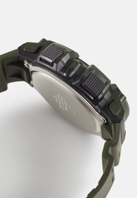 Montre numérique avec un boîtier en caoutchouc texturé noir et vert, un dos en acier inoxydable et des boutons-pression bien visibles pour la fonctionnalité.