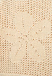 Un tissu tricoté beige doux présente un motif de fleur en relief avec cinq formes de pétales, mettant en valeur un motif texturé à armure ouverte.