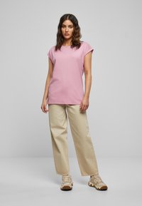 Pink short-sleeve T-shirt with a relaxed fit, paired with light beige wide-leg trousers and beige sneakers. Simple design with minimal accents.