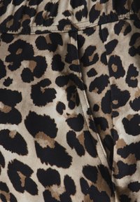 Tissu à motifs léopard présentant un mélange de tons beiges, noirs et marrons. Texture douce avec des coutures visibles, conçu dans un style plissé.