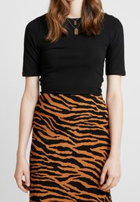 Černý top s krátkým rukávem v kombinaci s sukní s hnědým a černým tygřím pruhovaným vzorem, která má hladkou texturu a přiléhavý design.