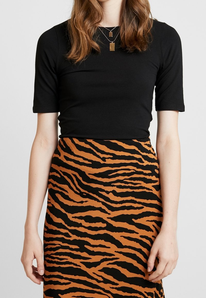 Černý top s krátkým rukávem v kombinaci s sukní s hnědým a černým tygřím pruhovaným vzorem, která má hladkou texturu a přiléhavý design.