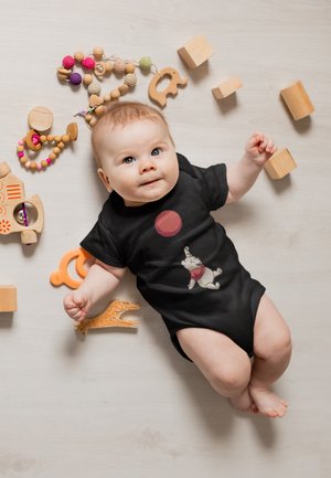 Black baby onesie featuring a cartoon bear and balloon design. Surrounding wooden toys include blocks and textured beads in various colors.