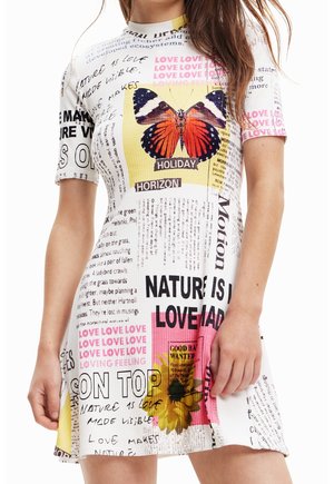 Femme portant une robe à manches courtes ornée de textes, d'un grand motif de papillon et de motifs floraux colorés.