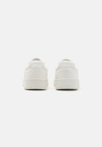 Weiße Sneaker mit einem glatten, synthetischen Obermaterial, runder Schuhspitze und gepolstertem Kragen. Minimalistisches Design mit dezenten Nähakzenten.