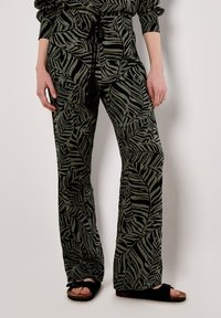 Green patterned trousers with a leaf design, elastic waistband featuring a drawstring, and wide-leg silhouette. Textured fabric with slight sheen.