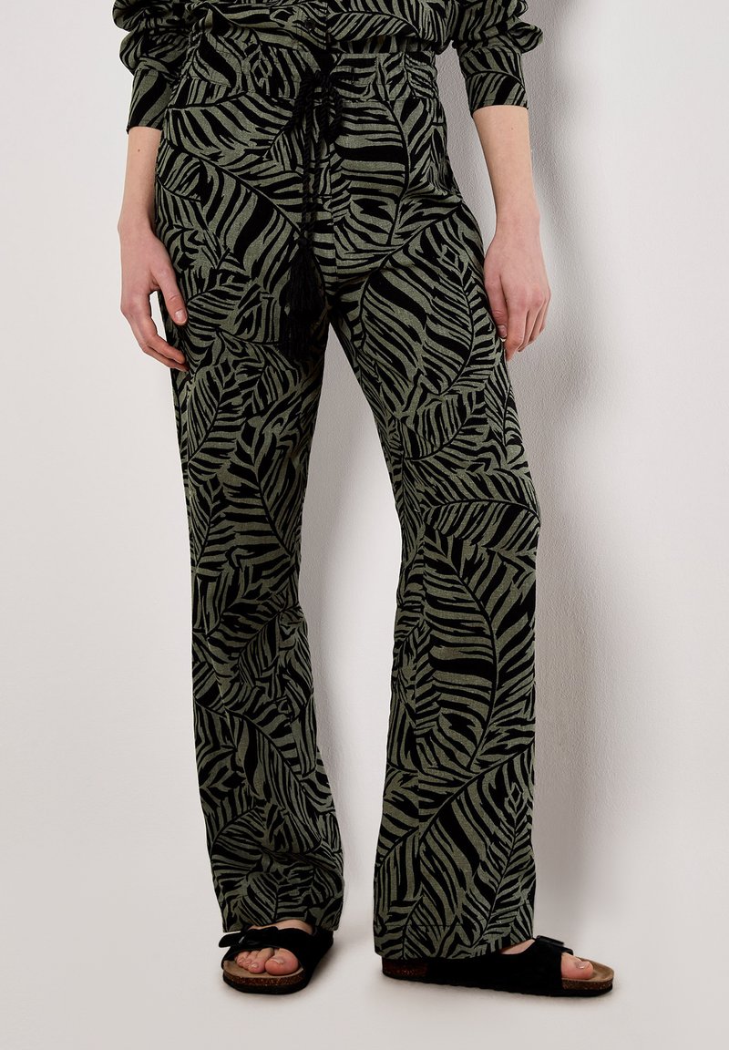 Green patterned trousers with a leaf design, elastic waistband featuring a drawstring, and wide-leg silhouette. Textured fabric with slight sheen.