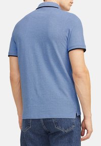 Blå polo t-shirt med korte ærmer, ribbet krave og sort kant. Båret sammen med mørke denimjeans. Tekstureret stof med en afslappet pasform.