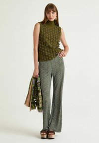 Top verde oliva senza maniche con motivo a rilievo, abbinato a pantaloni verde con fantasia a gamba larga. Scarpe con plateau, mantiene sciarpe dal design floreale.