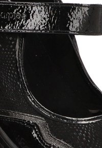 Zapato Mary Jane de charol negro brillante con patrón texturizado y correa ajustable en la parte superior.