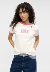 Κρεμ μπλούζα με ροζ ριμπ λάστιχο στο κολάρο και τα μανίκια, με έντονο ροζ γραφικό που γράφει "LOVE" πάνω σε σχέδιο τριαντάφυλλου.